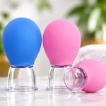 Beyaz havlu önünde mermer tezgahta pembe ve mavi silikon yüz masaj kupaları